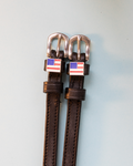 Brown leather ManeJane spur straps with American flag charms and rose-gold buckles