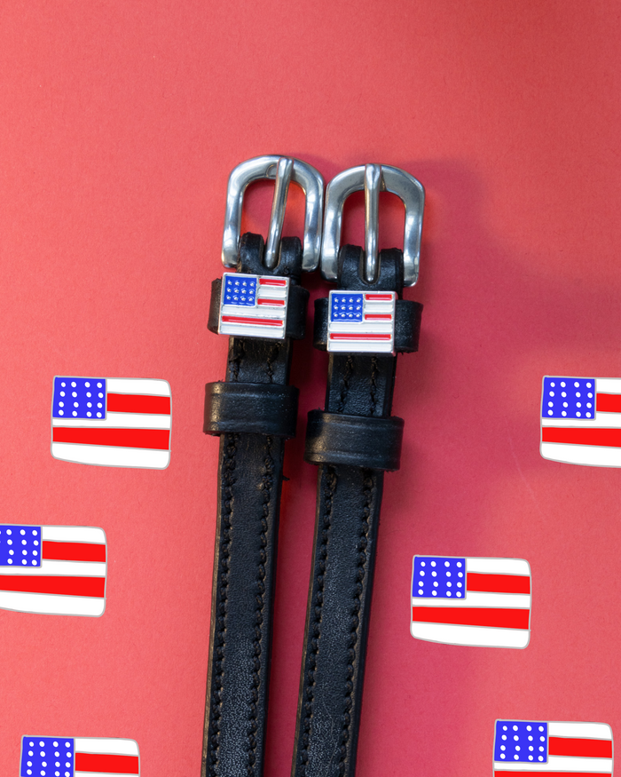 Black leather flag spur straps flat-laid on a red US flag icon backdrop