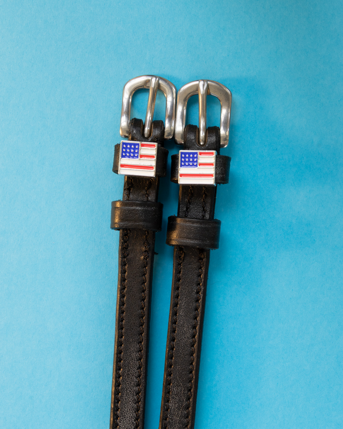 American flag spur straps in black leather on a light blue background
