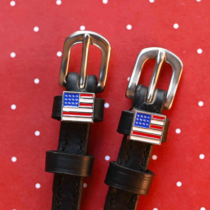 American flag charms and silver buckles on black spur straps, red polka-dot backdrop