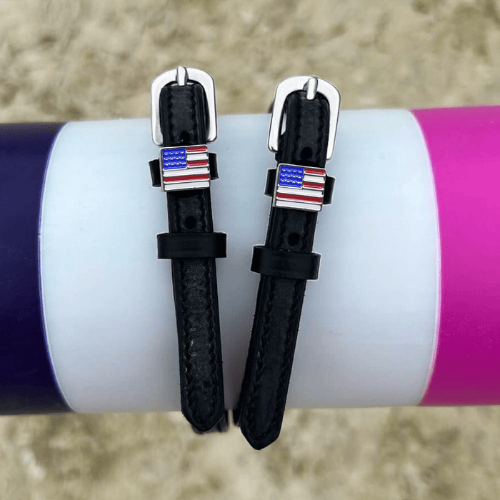 Black leather American flag spur straps draped over a colorful jump pole
