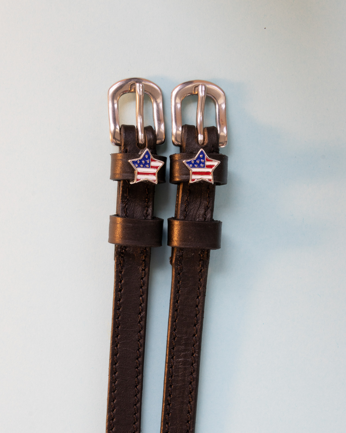 Brown leather American-flag star spur straps with rose-gold buckles, flat-lay
