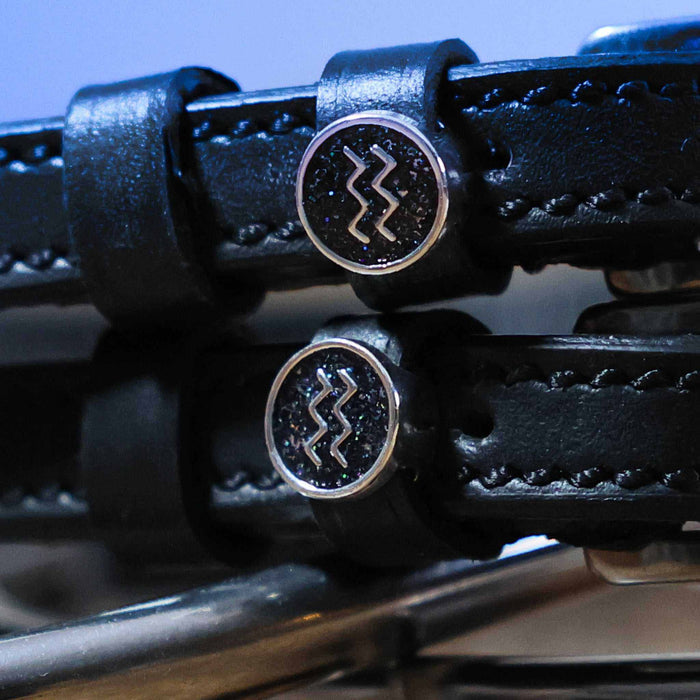 Close-up of round Aquarius zodiac medallion charms on black leather spur straps