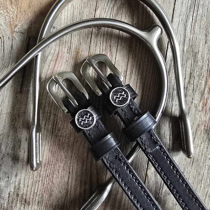 Black Aquarius zodiac spur straps flat-laid with a silver spur on weathered wood