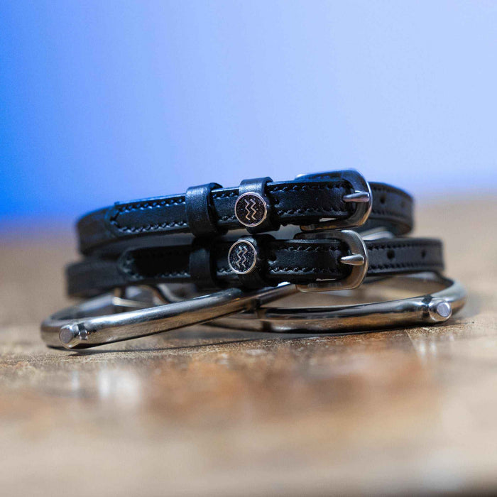 Aquarius charm spur straps coiled beside silver spurs on wood, blue backdrop