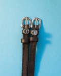 Black leather ManeJane spur straps with round Aries zodiac charms on a light blue background