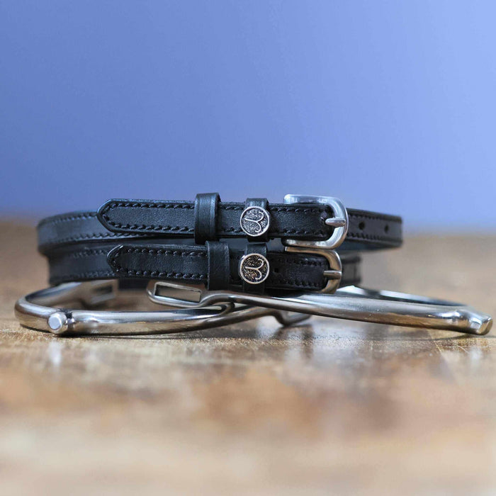 Black leather Aries zodiac spur straps coiled beside a silver spur on wood