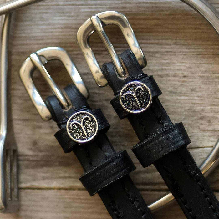 Macro of glittery Aries zodiac charms and silver buckles on black leather spur straps