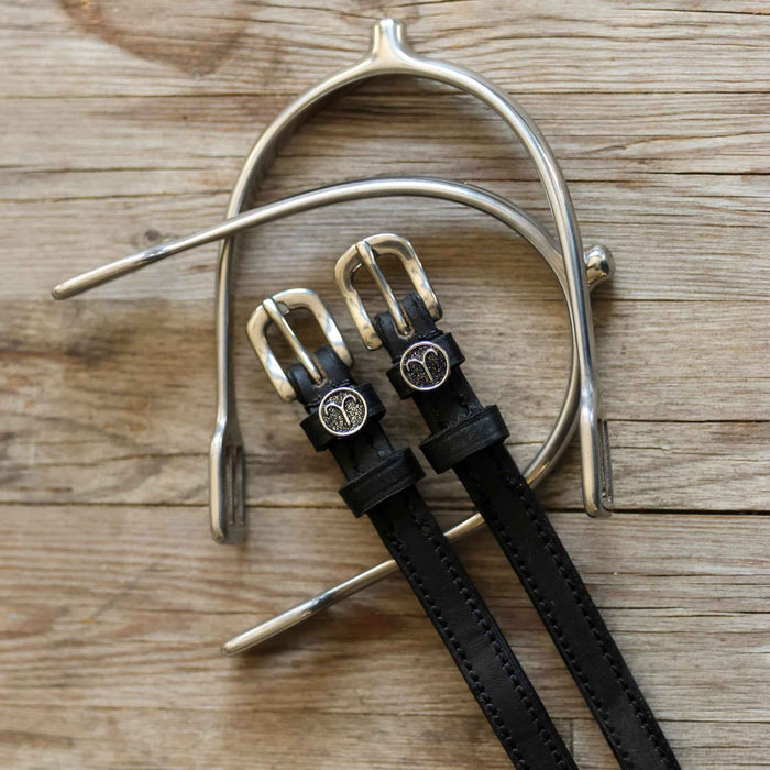 Black leather Aries zodiac spur straps arranged with a silver spur on rustic wood