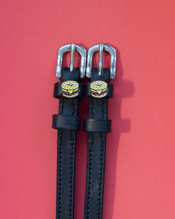 Pair of black leather ManeJane spur straps with bagel sandwich charms on pink