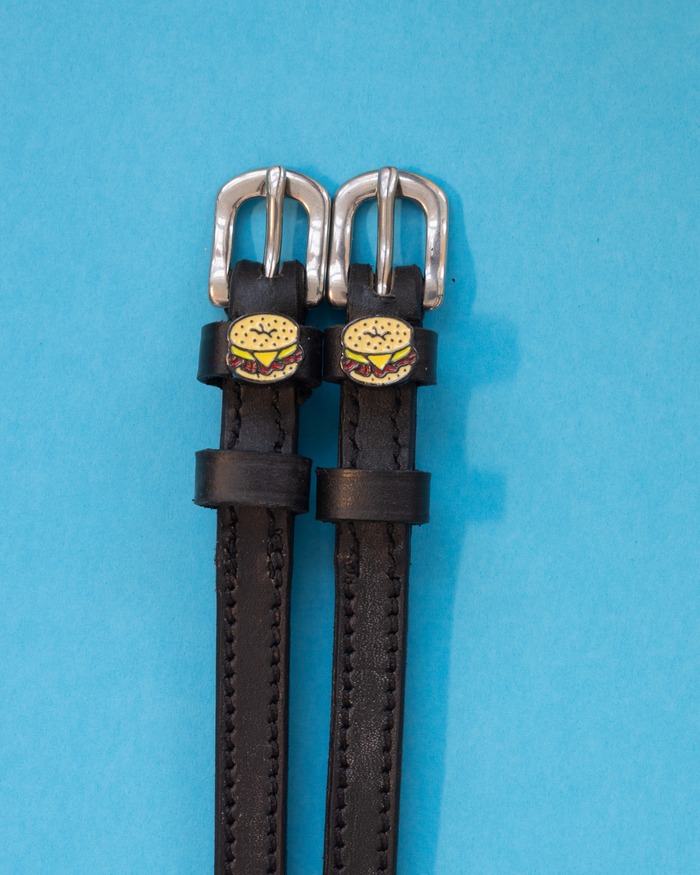 Black leather bagel sandwich spur straps flat-laid on a blue background