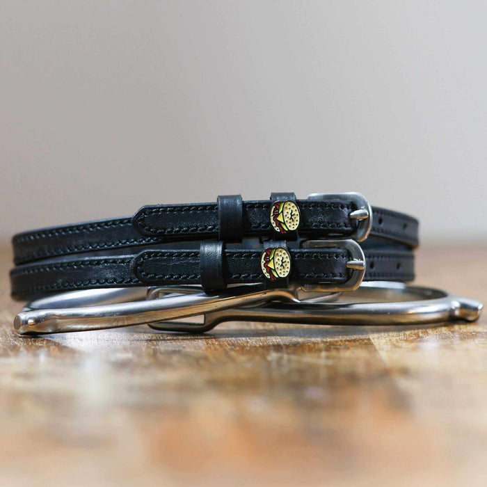 Black leather bagel sandwich spur straps coiled beside a spur on wood
