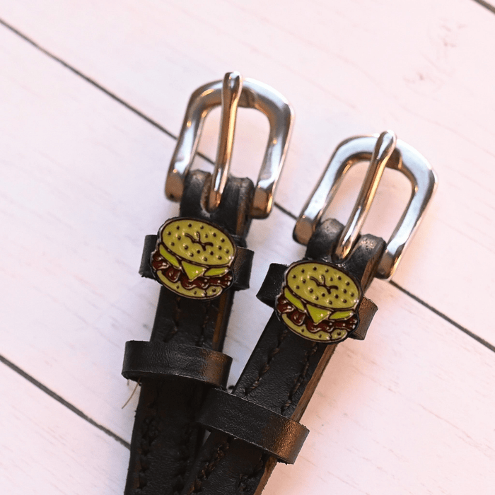 Two bagel sandwich charms on black leather spur straps over pink planks