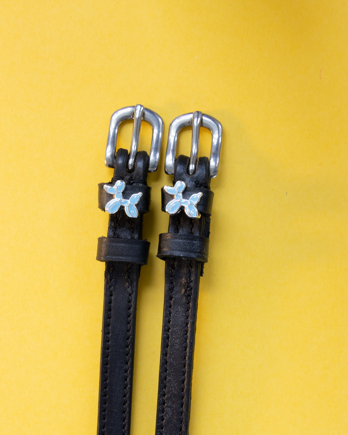 Black leather ManeJane spur straps with blue balloon dog charms on a yellow background