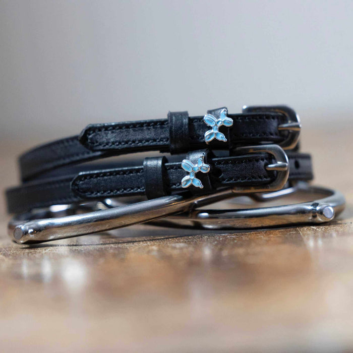 Black leather balloon dog spur straps coiled on wood beside a silver bit