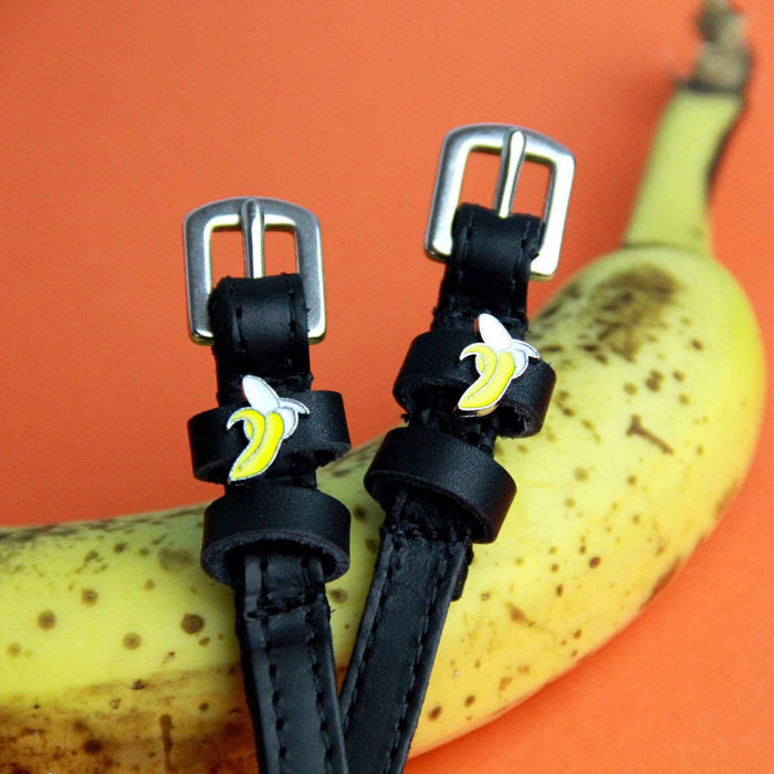 Banana spur straps styled beside a real banana on an orange background, silver buckles