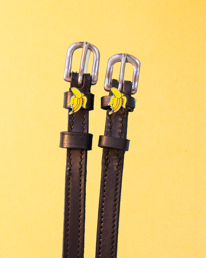 Dark brown leather banana charm spur straps with silver buckles on a yellow background