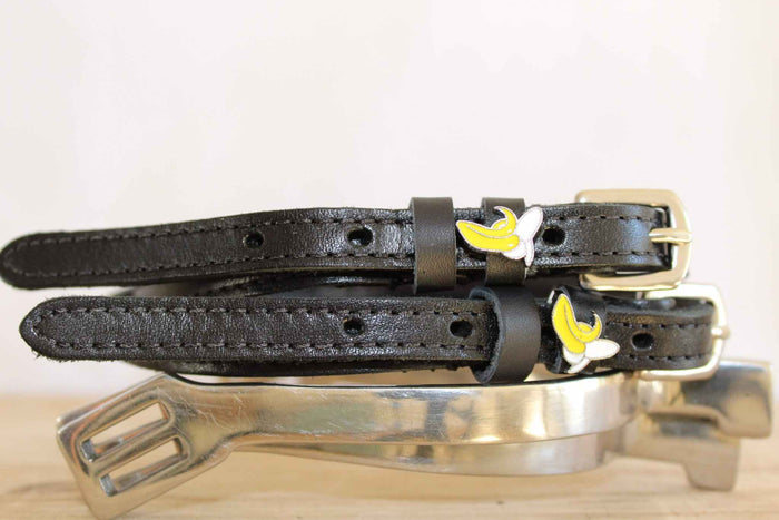 Banana spur straps coiled on silver spurs with a peeled banana charm on white