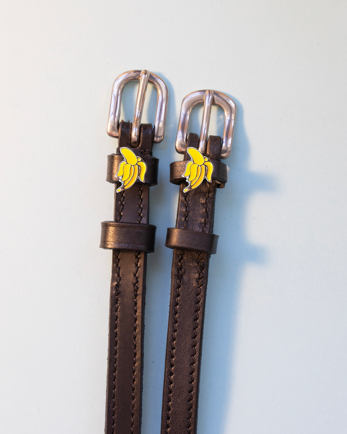 Dark brown Banana spur straps with silver buckles and banana charms on pale grey