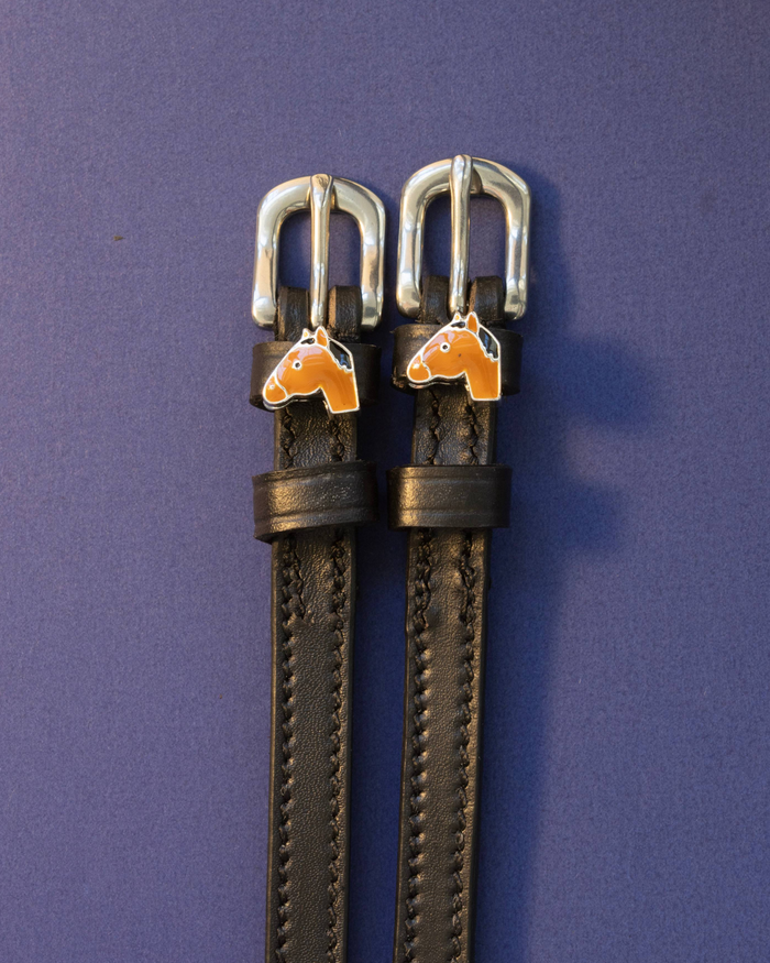 Bay horse-head charm spur straps in black leather on a blue-violet background