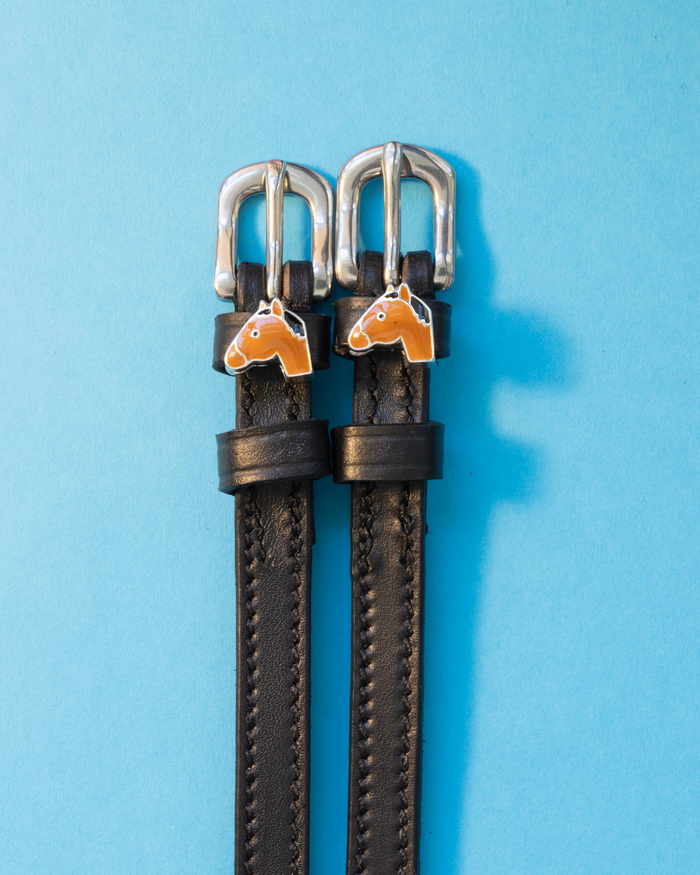 Pair of black leather horse-head spur straps laid flat on a light blue background