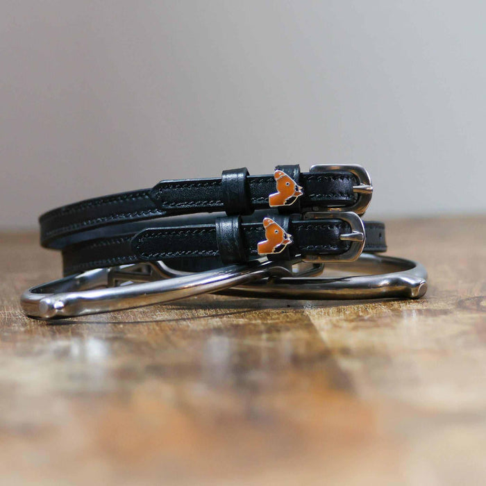 Coiled black leather spur straps and a silver spur on wood with horse-head charms