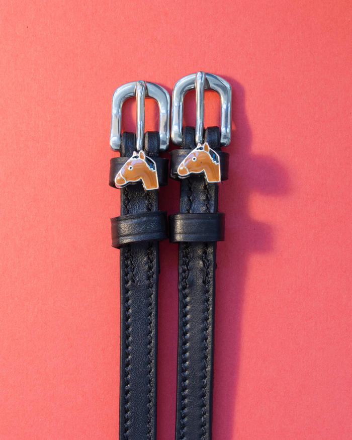 Black leather bay horse spur straps on a coral-red background with silver buckles