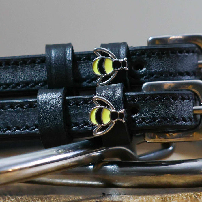 Close-up of silver-and-yellow bee charms on black leather ManeJane spur strap keepers