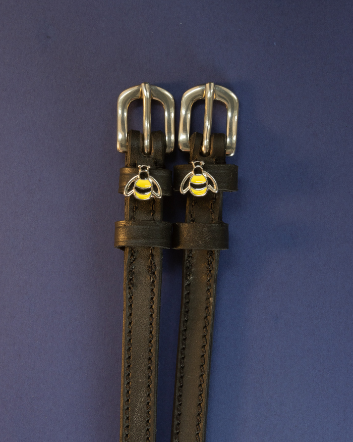 Pair of black leather bee spur straps with silver buckles laid flat on a navy blue background