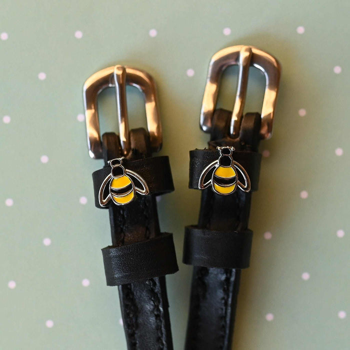 ManeJane bee charm spur straps with rose-gold buckles on a sage green polka-dot background