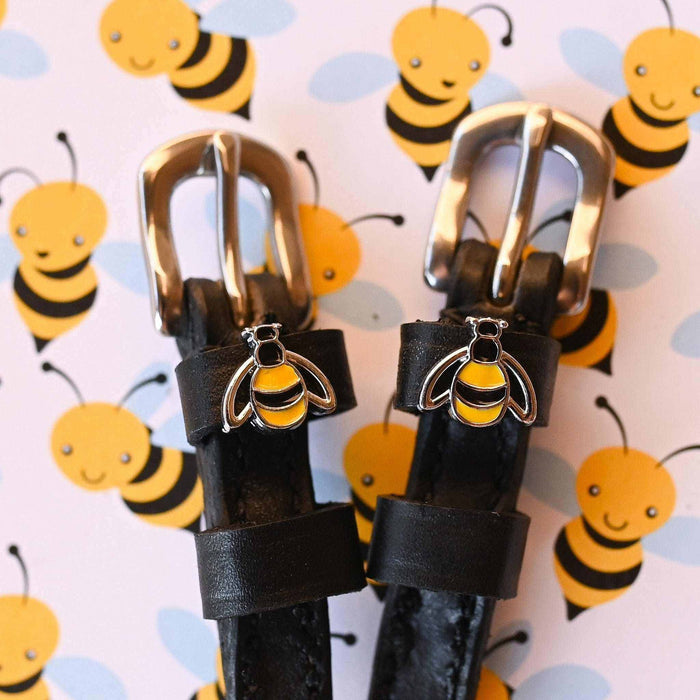 Bumblebee charms on black leather spur straps against a cartoon bee print backdrop