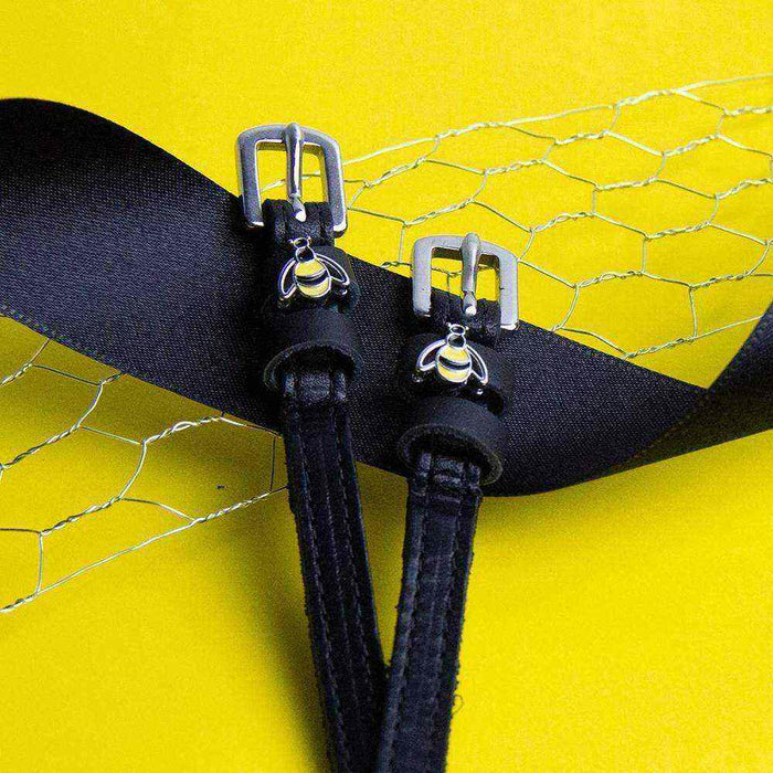 Bee spur straps buckled and fastened, bumblebee charms visible, on a yellow backdrop