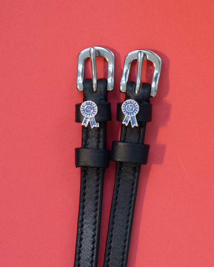 Pair of black leather blue-ribbon spur straps with silver buckles on a red background
