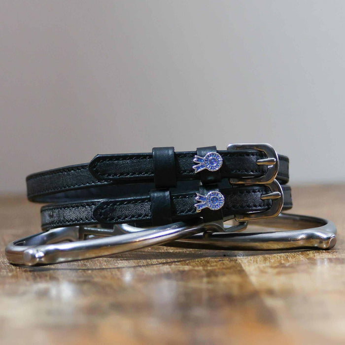 Blue ribbon spur straps coiled on a silver stirrup on a wooden table