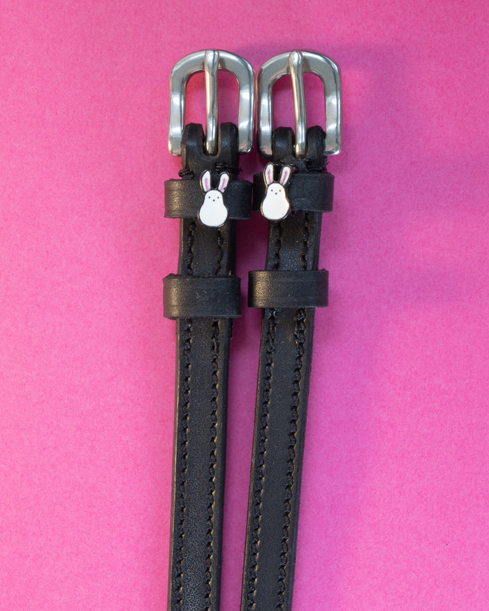 Black leather ManeJane Bunny Hop spur straps with white bunny charms on a hot pink background