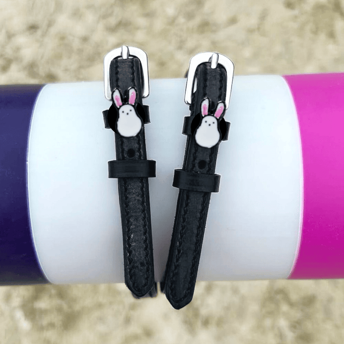 Bunny Hop spur straps wrapped around a tumbler on sand, white ManeJane bunny charm