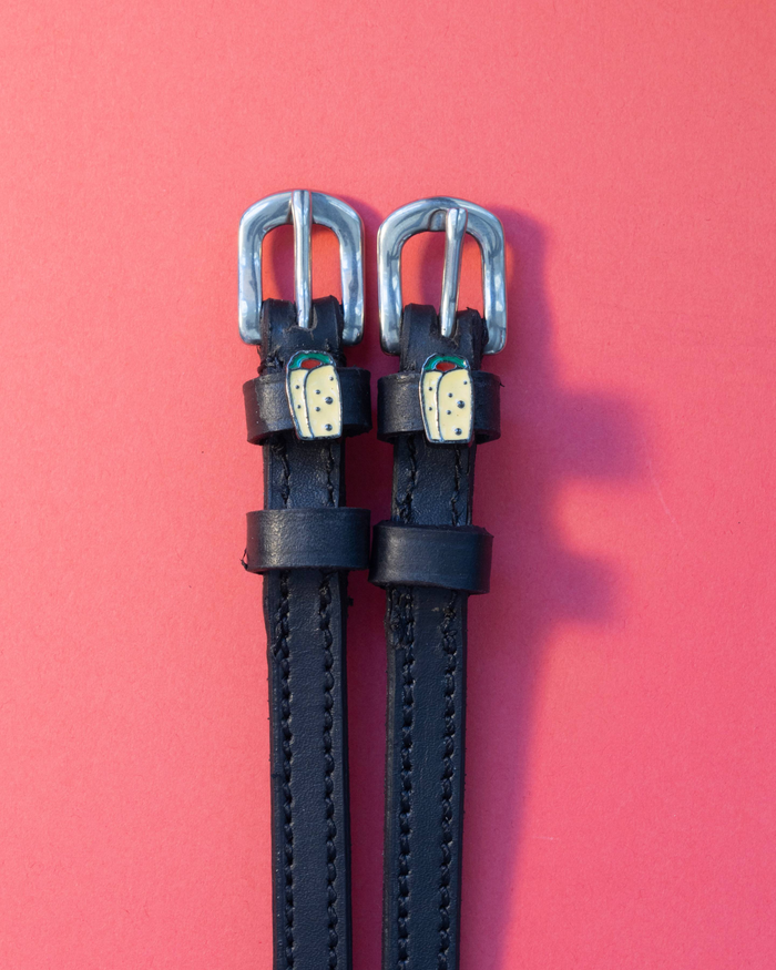 Black leather ManeJane spur straps with enamel burrito charms on a coral background