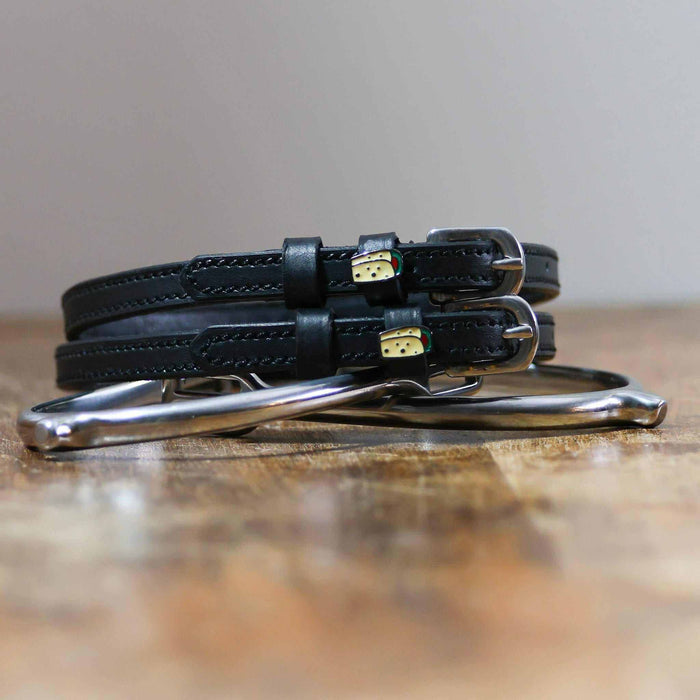 Coiled black leather burrito spur straps stacked on a silver spur on a wooden table