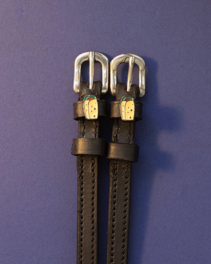 Black leather ManeJane burrito spur straps with silver buckles on a deep purple background