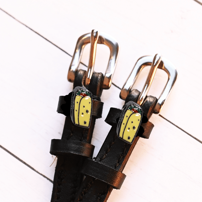 Overhead of black leather spur straps with silver buckles and burrito charms on white wood