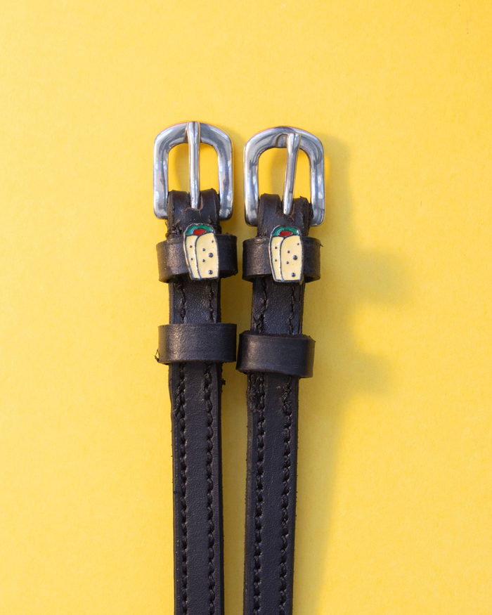 Black leather burrito spur straps with silver buckles on a yellow background by ManeJane