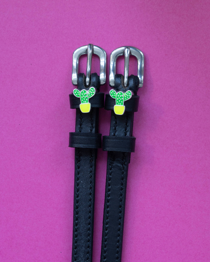 Black leather ManeJane spur straps with green potted cactus charms on a magenta background