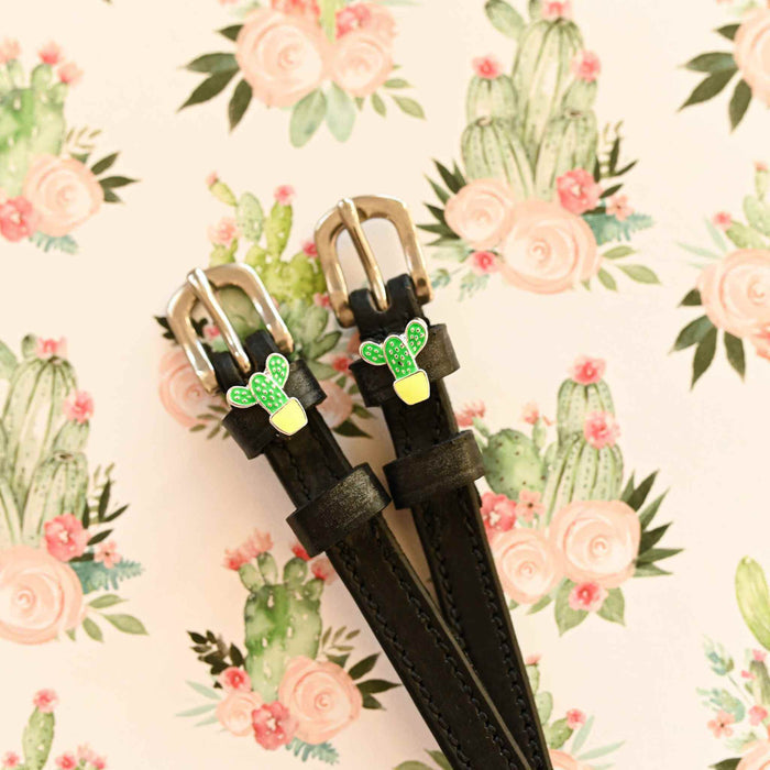 Pair of cactus charm spur straps laid on a floral cactus print background