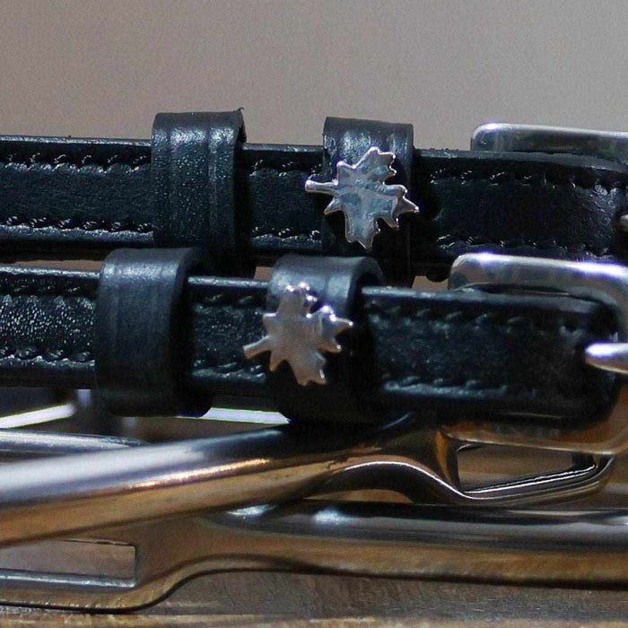 Close-up of silver maple leaf charms on black leather ManeJane spur straps over spur hardware