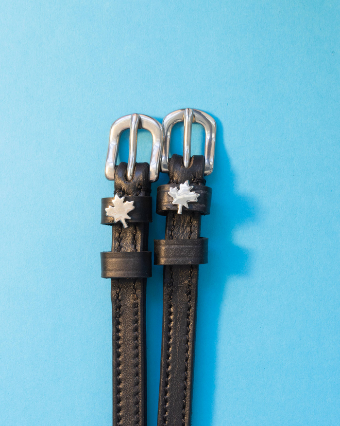 Pair of black leather maple leaf spur straps with silver buckles on a light blue background