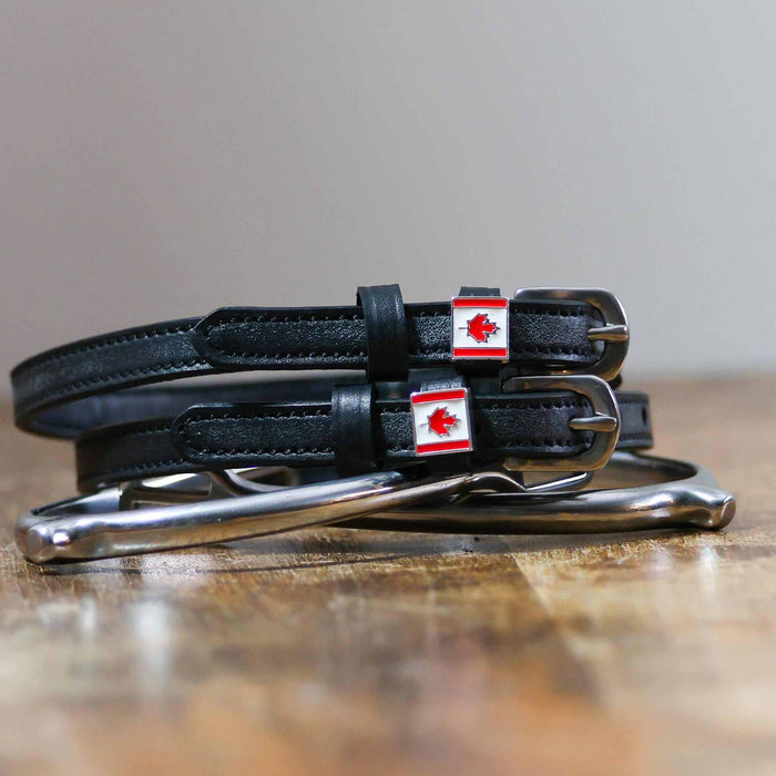 Black leather Canadian flag spur straps coiled beside a stirrup on a wooden surface