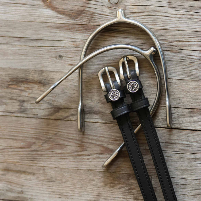 Overhead of black leather Cancer zodiac spur straps beside a silver spur on weathered wood