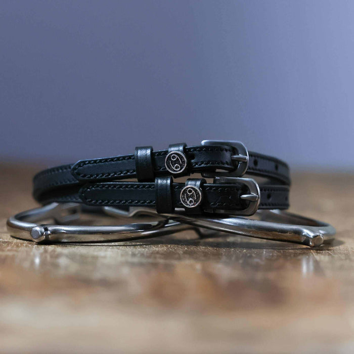 Coiled black leather ManeJane Cancer zodiac spur straps stacked on a silver spur on wood