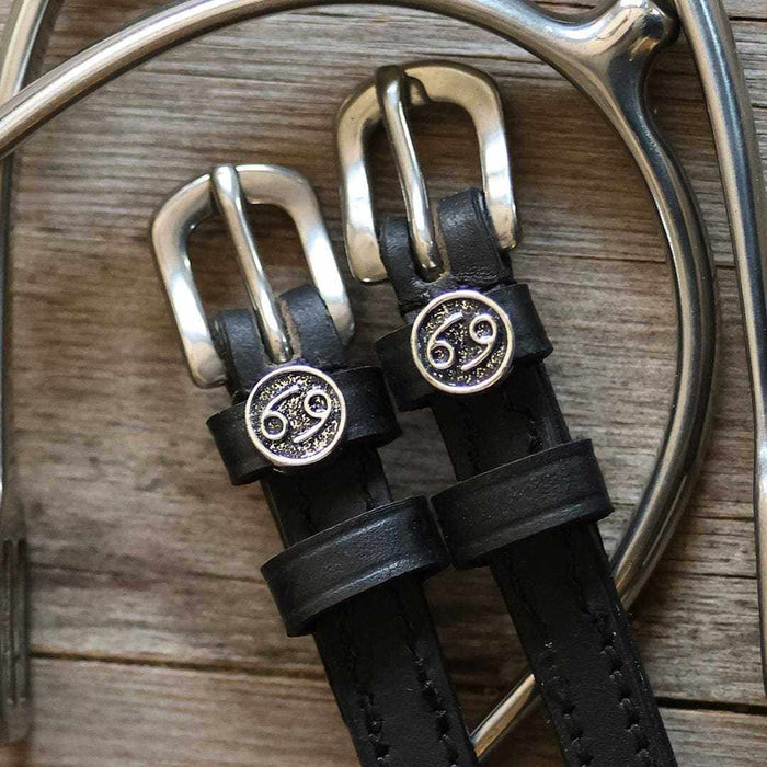 Silver buckles and Cancer zodiac charms on black leather spur straps over a spur and wood