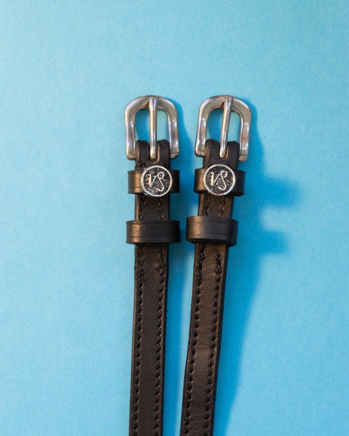 Black leather ManeJane spur straps with round Capricorn zodiac charms on light blue